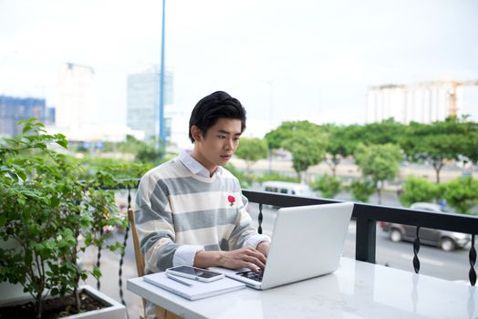 Asian young business man working with laptop at the city cafe.