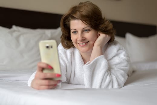 A woman in a bathrobe wears a telephone in the hotel room