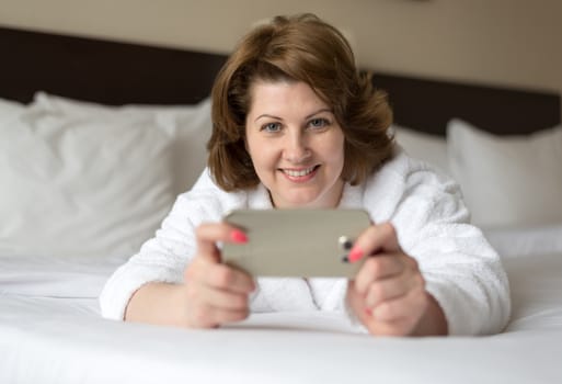 A woman in a bathrobe wears a telephone in the hotel room
