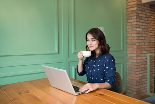 Beautiful cute asian young businesswoman in the cafe, using laptop and drinking coffee smiling