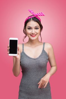 Beautiful young asian woman with pin-up make-up and hairstyle over pink background with mobile phone