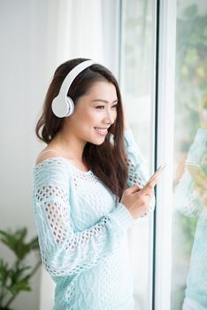 Asian woman enjoying view on windowsill and listening to music.