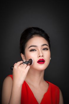 Cosmetic powder brush. Asian woman applying blusher on her cheeks with perfect make-up and red lips