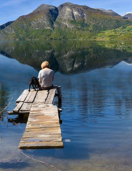 Woman with dog sitting on bridge by the lake in the mountains