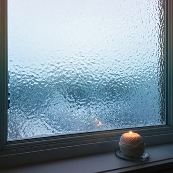 Blue frosted window and cozy candlelight. Winter composition.