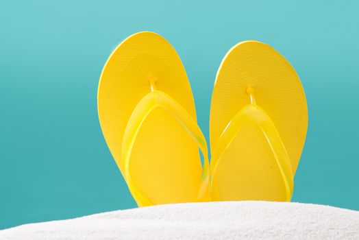 Yellow flip flops on beach against blue background.