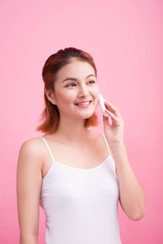 Young lady applying blusher on her face with powder puff, skin care concept on pink background.