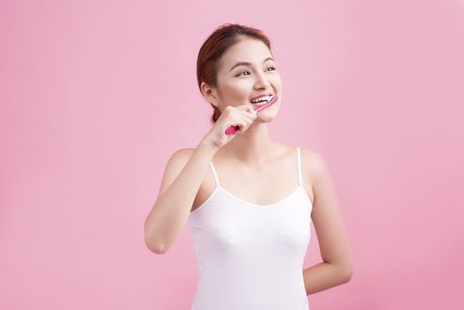 Smiling young woman with healthy teeth holding a tooth brush over pink background.