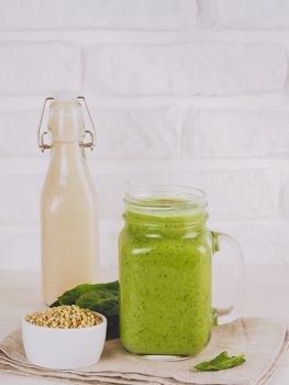 Close up view of green smoothie in mason jar on white table. Fresh green smoothie with green buckwheat, spinach and vegan milk. Copy space. Vertical.