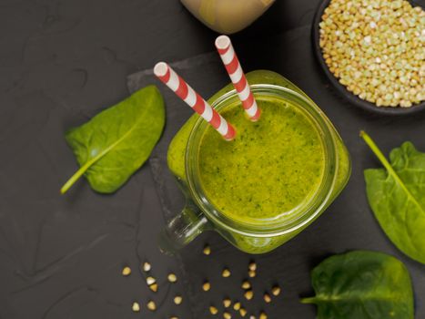 Top view of green smoothie in mason jar on black concrete background. Fresh green smoothie with green buckwheat, spinach and vegan milk. Copy space. Vertical.