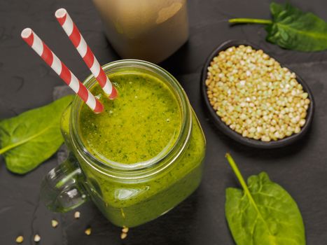 Top view of green smoothie in mason jar on black concrete background. Fresh green smoothie with green buckwheat, spinach and vegan milk. Copy space. Vertical.