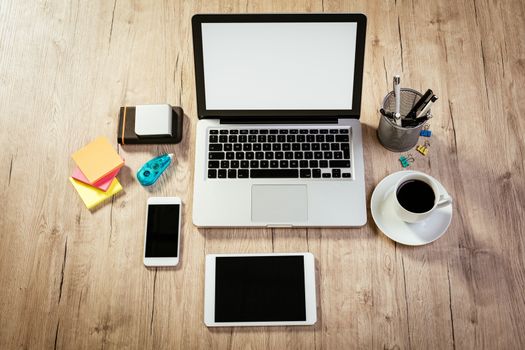 Top view of a workspace with laptop, digital tablet and smartphone with blank screen. Different office accessories and cup of coffee is on the table. 