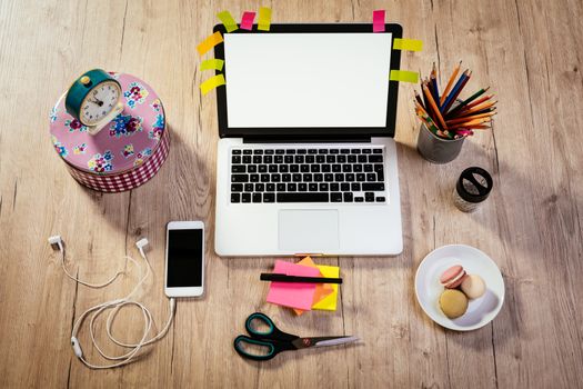 Top view of a workspace with laptop, digital tablet and smartphone with blank screen. Different office accessories and franch macaroons is on the table. 