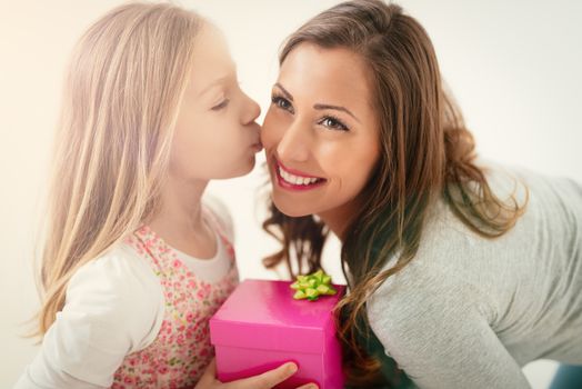 Cute little girl kissing and giving small pink gift box for her smiling mom. Selective focus.