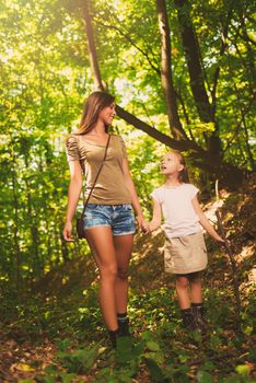Beautiful young mother and her daughter talking and walking through forest. 