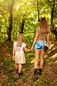 Beautiful young mother and her daughter walking through forest. Rear view.