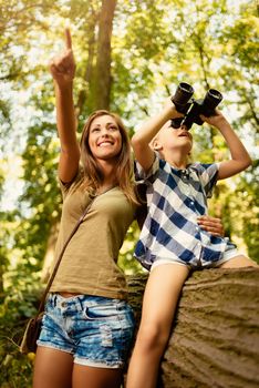 Beautiful young family having fun in the forest. Little girl exploring thru binoculars, her mother pointing with finger far away.