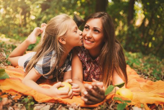 Beautiful mom and her little girl is lying in a forest and enjoying. Little girl kissing young woman.