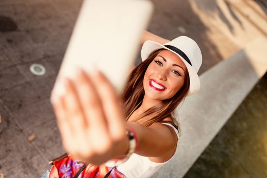 Beautiful young woman with hat taking selfie on the street.