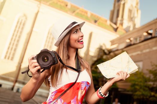 Beautiful young worried woman on vacation walking on the city and holding map of city and digital camera.