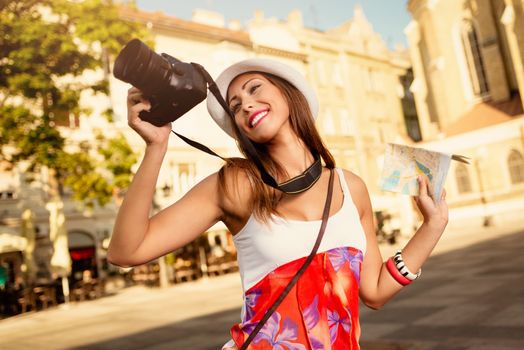 Beautiful young girl tourist holding map and photographing with digital camera.