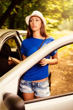 Confused pensive beautiful woman standing leaning at car in the forest and worried looking a map.