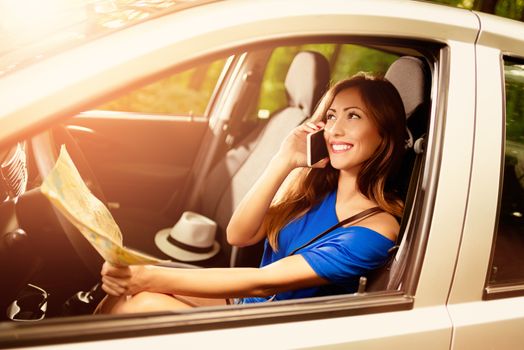 Young beautiful woman sitting in car, talking at the smart phone and holding map.