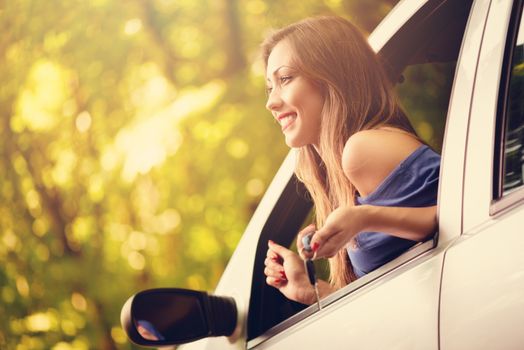Young beautiful woman sitting in car in the forest and looking next direction. She is holding car keys and looking away.