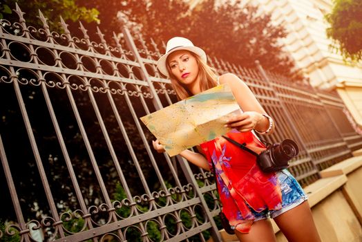 Cute smiling young woman on vacation walking on the city and studying map. She is have a digital camera.