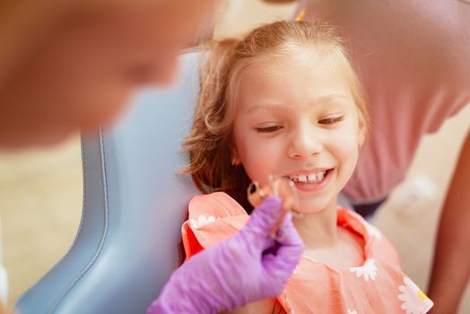 Close-up of a dentist showing mobile orthodontic appliance the little girl patient. Selective focus. Focus on background, on little girl.