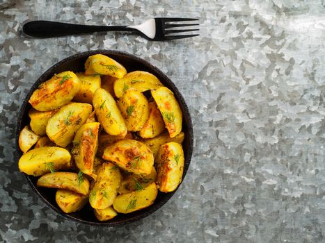 Top view of baked potatoes in cast iron skillet with black fork on gray galvanized iron background. Copy space.