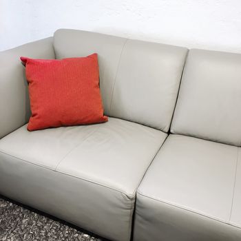 Red cushion decorating a simple gray leather sofa.