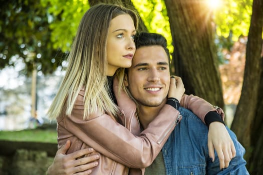 Boyfriend and girlfriend standing in countryside in green luscious field, embracing each other and cuddling, showing romantic love