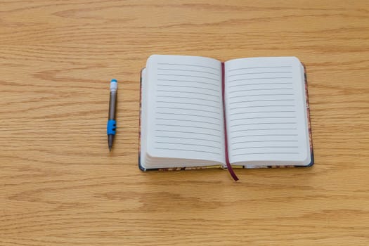 A pencile beside a notebook with blank pages on a table.