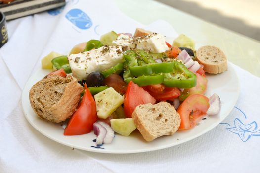 Plate of Greek salad with tomatoes, onions, peppers, feta, bread.