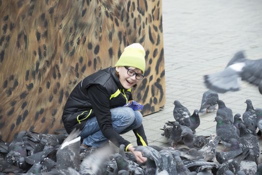 Girl feeds pigeons on the city square on a background of graffiti
