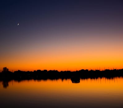 A crescent moon seen over a northern lake at sunset