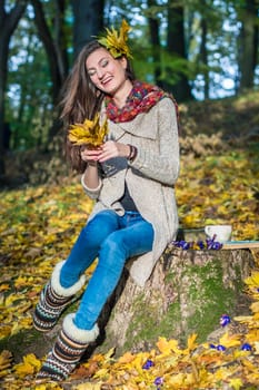 smiling, happy girl sitting on a stump in the autumn park