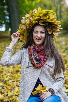 smiling, happy girl wearing a wreath of maple leaves in autumn park