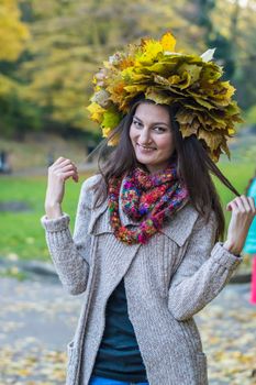 smiling, happy girl wearing a wreath of maple leaves in autumn park