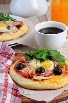 Mini pizza with sausage and egg and arugula, a cup of coffee 