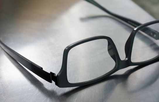 COLOR PHOTO OF PLASTIC FRAME GLASSES ON STEEL TABLE