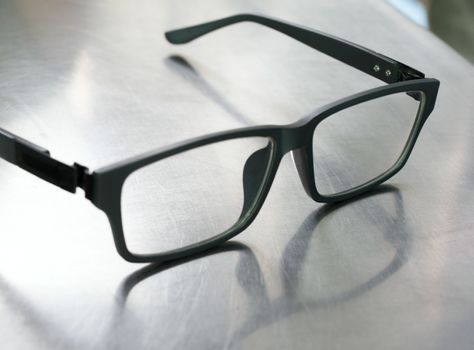 COLOR PHOTO OF PLASTIC FRAME GLASSES ON STEEL TABLE