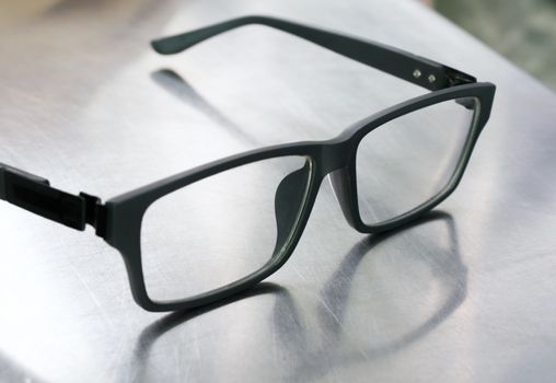 COLOR PHOTO OF PLASTIC FRAME GLASSES ON STEEL TABLE