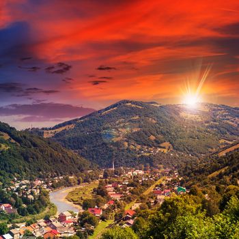 autumn landscape. village by the river. light fall on forest on mountains in evening