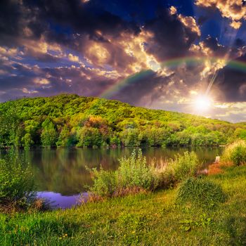 view on lake near the pine forest with rainbow late in evening on mountain background