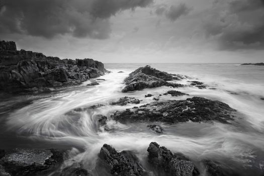 Seascape at low tide with moody clouds and pending storms and swirling ocean currents around the exposed rocks.