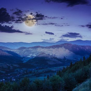 autumn landscape. village on the hillside. forest on the mountain light fall on clearing on mountains at night in moon light