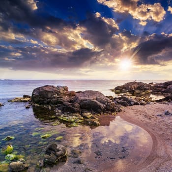 sea wave attacks the boulders and is broken about them at sunset