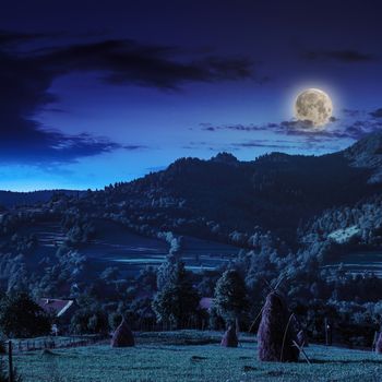 Stack of hay on a green meadow in the mountains in the morning under a blue summer sky at night in moon light